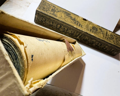Vintage piano roll with cream-colored paper case and ornate gold-stamped spine displayed partially unrolled against white