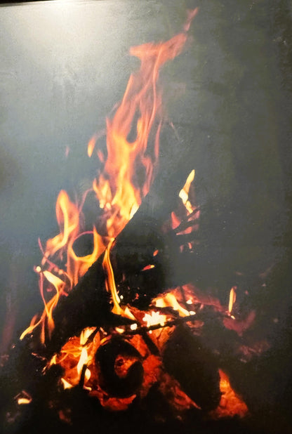 Vibrant bonfire flames in yellow, orange, and red against dark smoke and night sky, framed photograph
