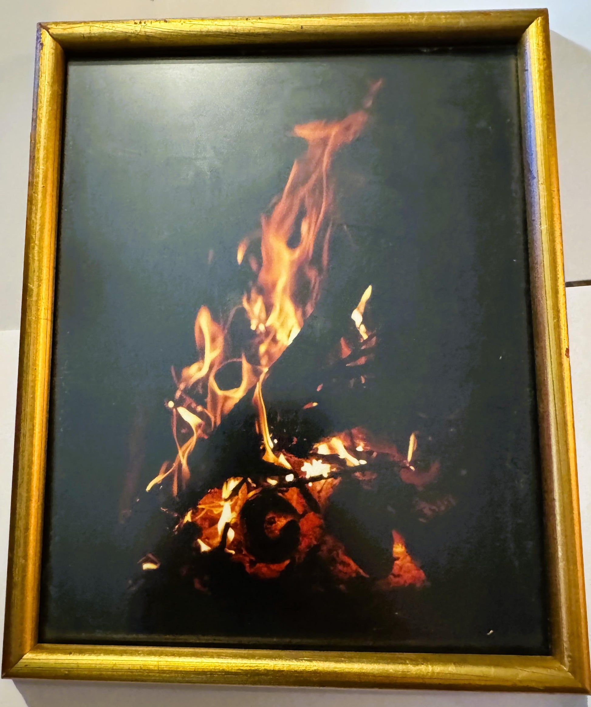 Framed color photograph of a bonfire with bright yellow and orange flames against dark background, gold-tone frame, mounted o