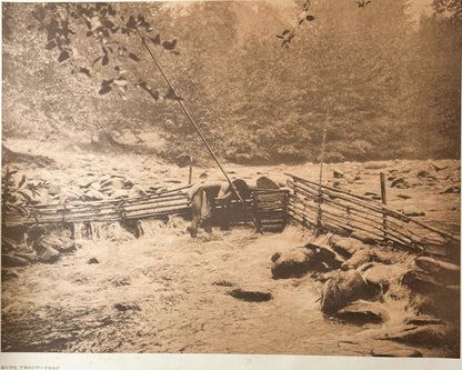 Sepia-toned photogravure showing a wooden fish trap structure spanning a rocky stream, with wooden fencing and forest backdro