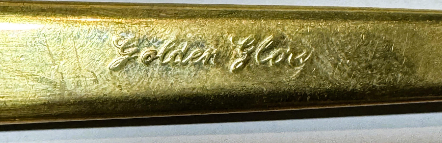 Close-up of embossed gold-tone brass flatware handle showing cursive script text against textured surface