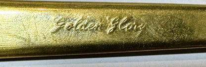 Close-up of embossed gold-tone brass flatware handle showing cursive script text against textured surface