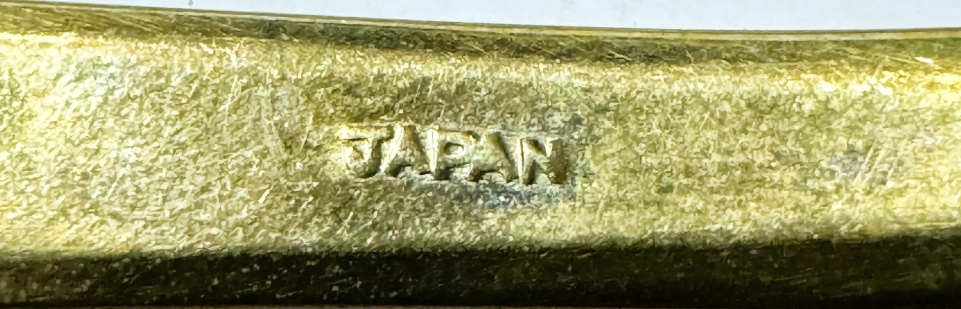 Close-up of embossed "JAPAN" marking on textured gold-tone brass flatware handle