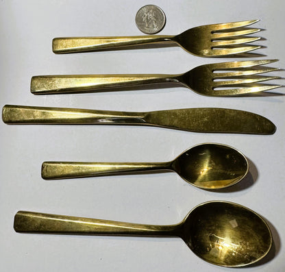 Five brass flatware pieces arranged vertically with a quarter coin at top for scale, showing two forks, knife, and two spoons