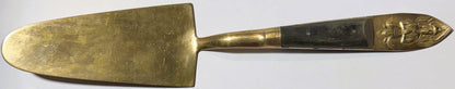 Antique brass serving knife with decorative Thai deity handle, shown against white background from above