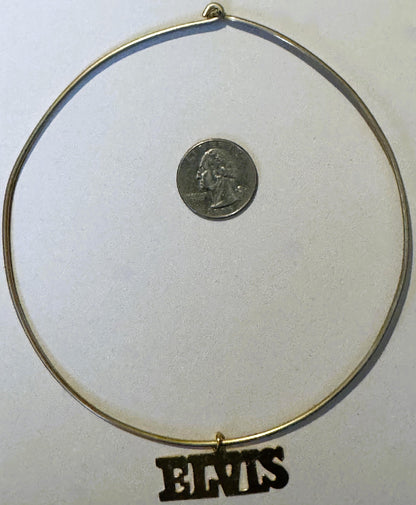 Gold-tone choker necklace with quarter coin for scale, black "ELVIS" nameplate charm pendant at bottom