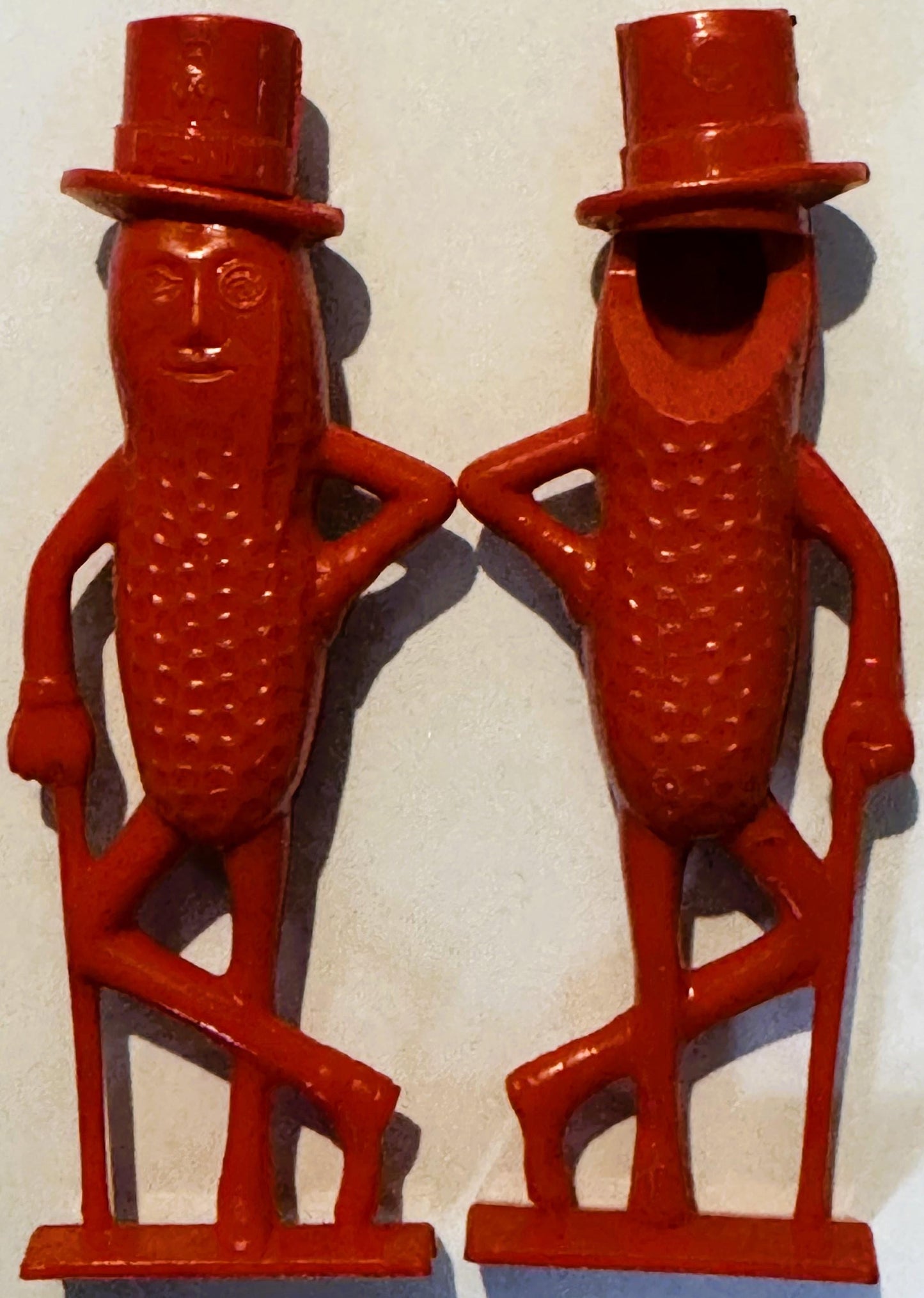 Two red plastic Mr. Peanut figurines with top hats, monocles, and dotted bodies shown front and back against white background