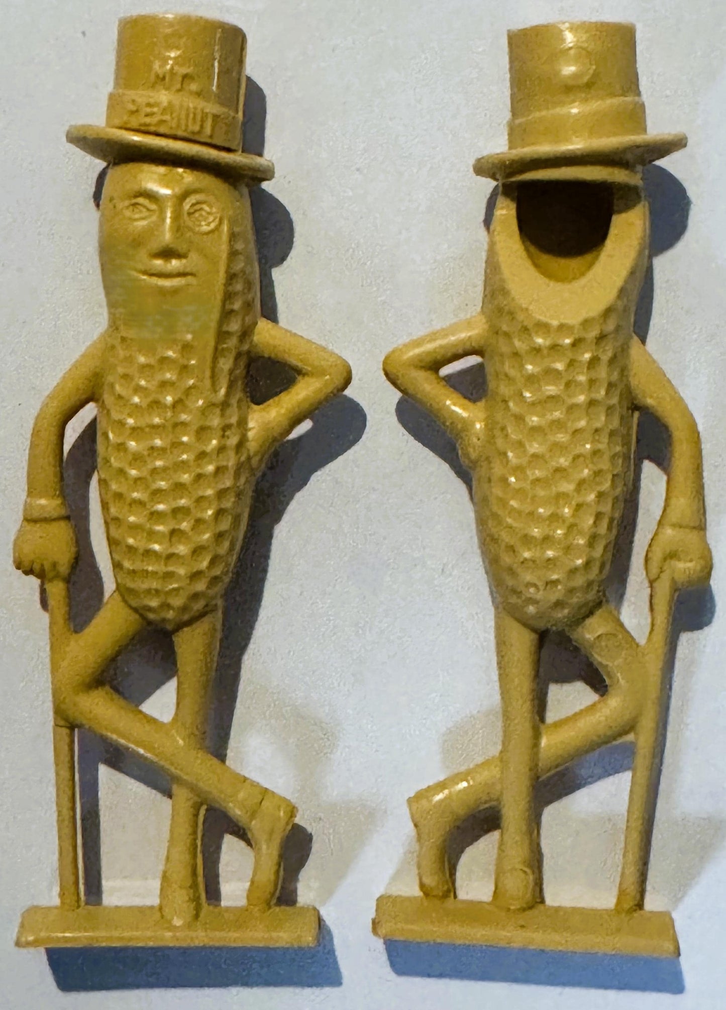 Front and back views of yellow plastic Mr. Peanut figurines with top hats, monocles, and canes, featuring embossed corn cob b