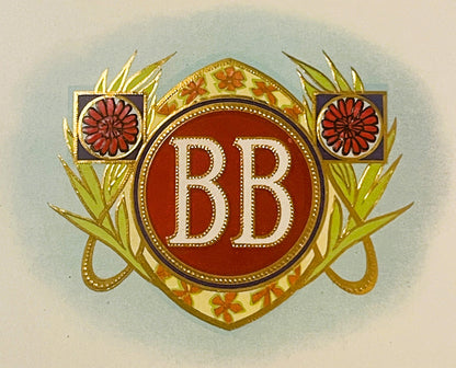 Antique gold-embossed cigar label close-up: white BB monogram on a red medallion in a gold frame, red flowers in purple squares on each side, green leaves, on a pale blue haze.