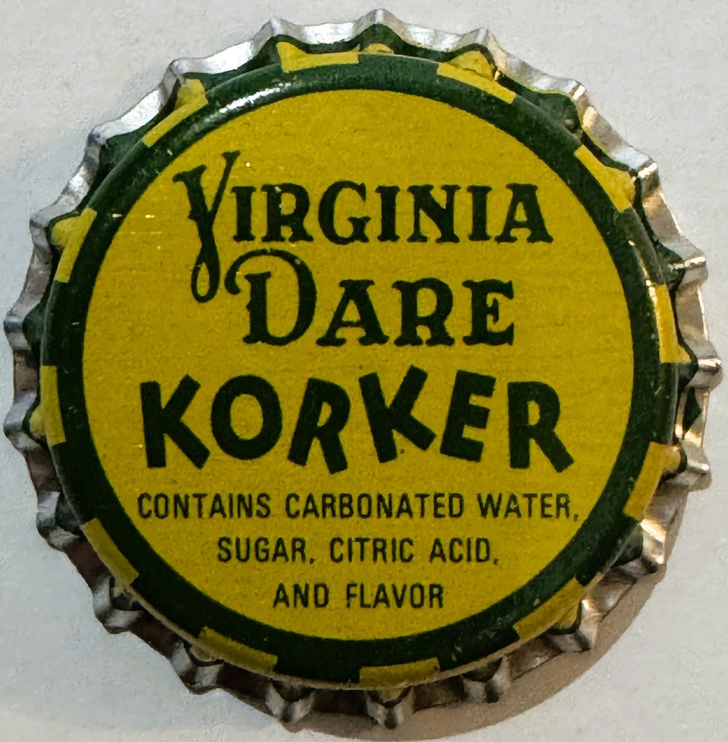 Vintage bottle cap with yellow center and green border, printed "Virginia Dare Korker" with ingredients text, viewed flat aga