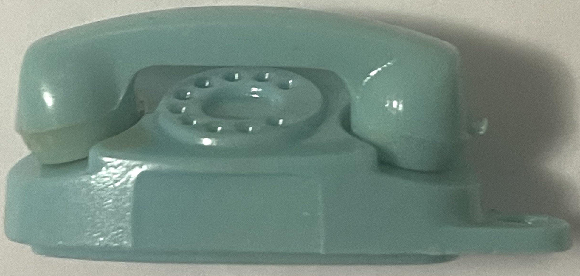 Teal plastic miniature rotary telephone keychain charm shown from above against white background, displaying numbered dial pa