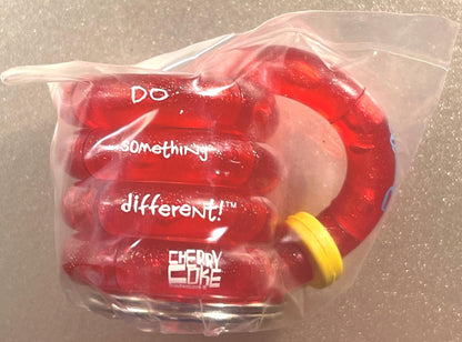 Sealed clear plastic package containing red Cherry Coke branded fidget toy with yellow band, printed text visible including "