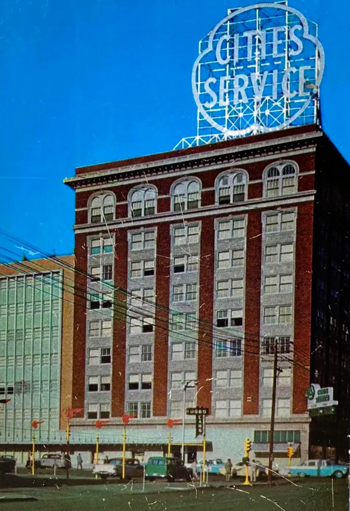 Vintage neon "Cities Service" sign atop red brick building against blue sky, 1980s photograph