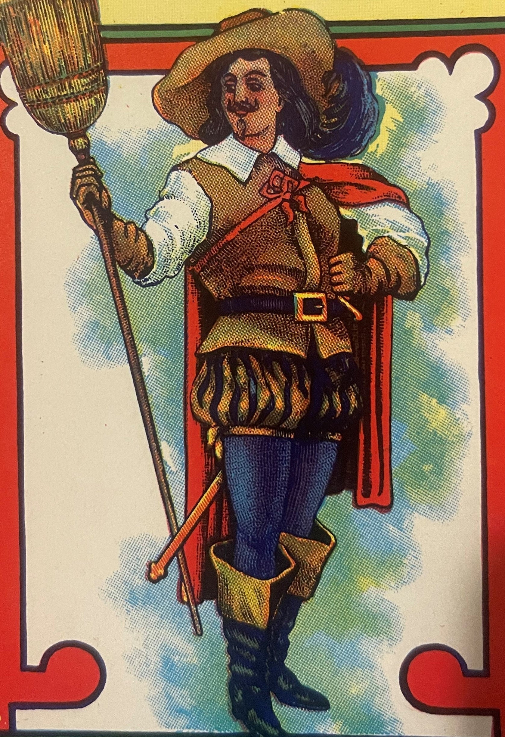 Colorful lithographed broom label featuring a bearded cavalier in red cape and feathered hat holding a broom, with red border