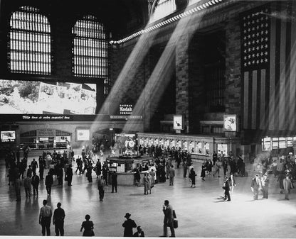 Black and white photograph of Grand Central Terminal's main concourse with crowds of people, dramatic light rays, and America