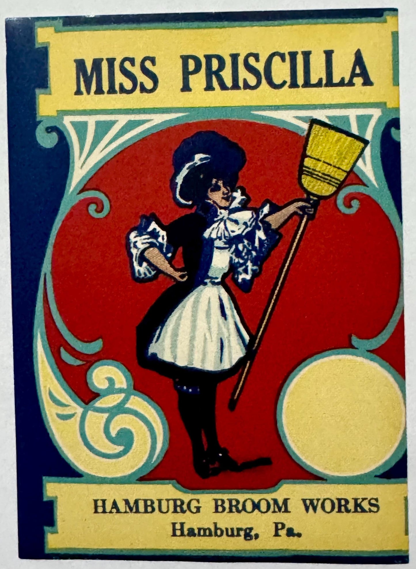 Vintage broom label featuring woman in maid outfit holding yellow broom against red background.