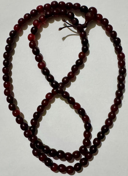Antique Republic China horn bead necklace laid in a figure eight on white, deep cherry red beads with the head bead and cord tails at the top