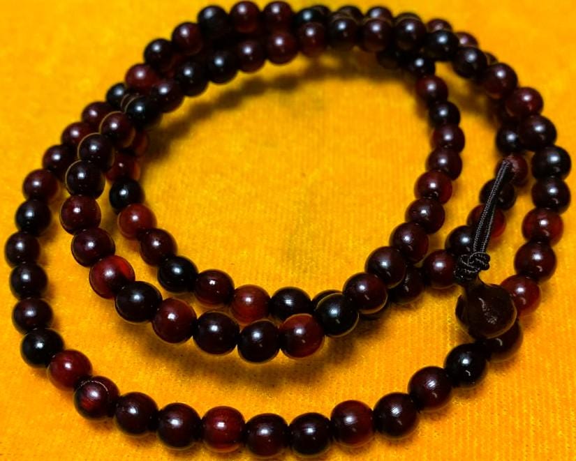 Close-up of the horn beads coiled on a yellow cushion, showing the bead grain and the gourd-shaped head bead tied off with a decorative knot