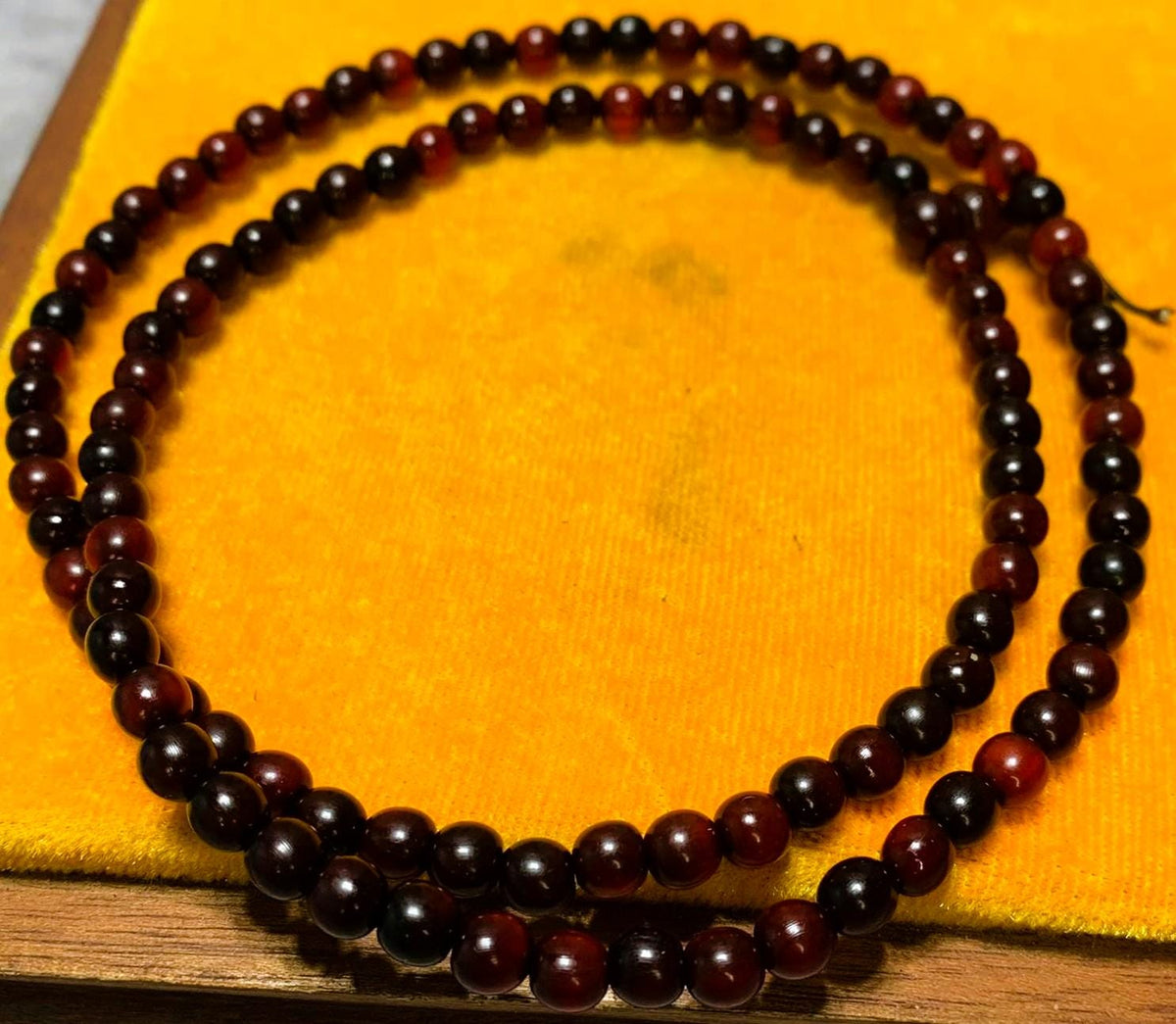 The cherry red horn bead strand coiled in two loops on a yellow cushion stand