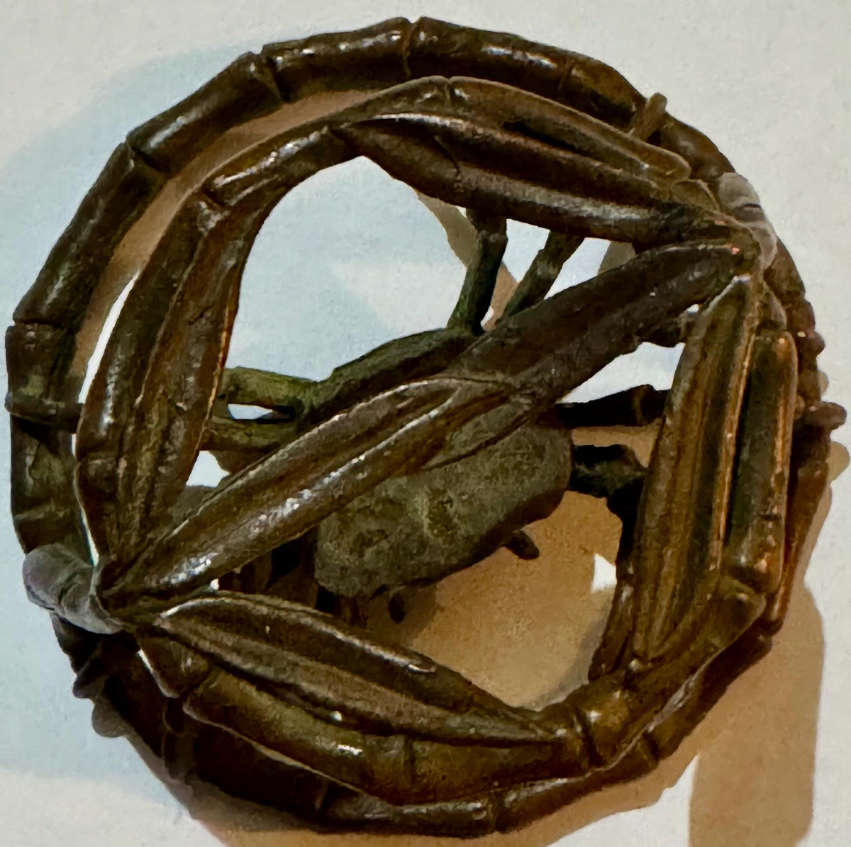 Bronze crab sculpture with intertwined limbs within a segmented circular ring frame.