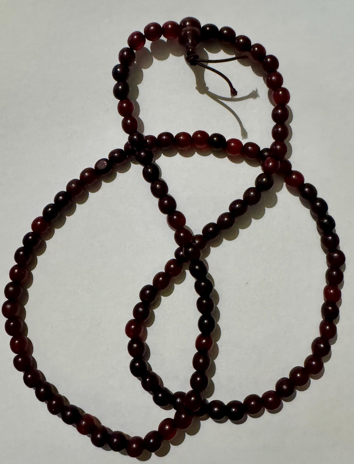 Horn bead necklace laid in overlapping loops on white, dark cherry red beads, with the head bead and two cord tails at the top.