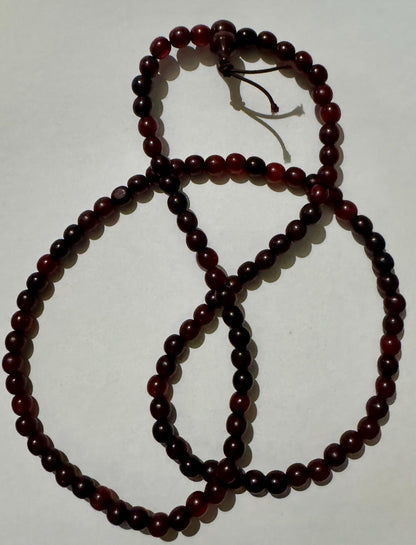 Horn bead necklace laid in overlapping loops on white, dark cherry red beads, with the head bead and two cord tails at the top.