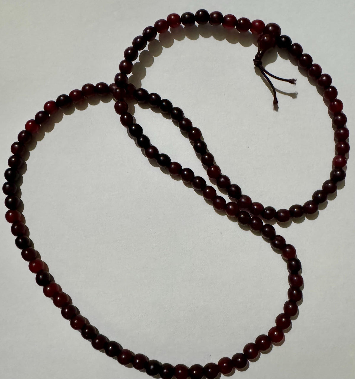 Horn bead necklace laid in two overlapping loops on white, deep red to near-black beads, with the head bead and cord tails at upper right.
