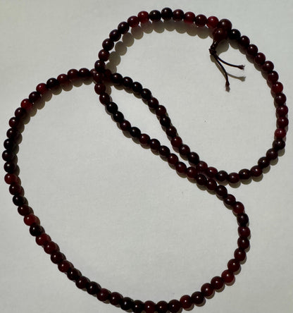 Horn bead necklace laid in two overlapping loops on white, deep red to near-black beads, with the head bead and cord tails at upper right.