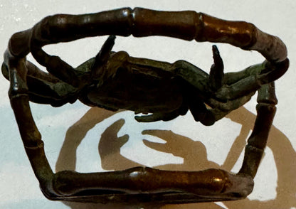 Bronze crab with green patina mounted in bamboo-style ring frame, viewed from above.
