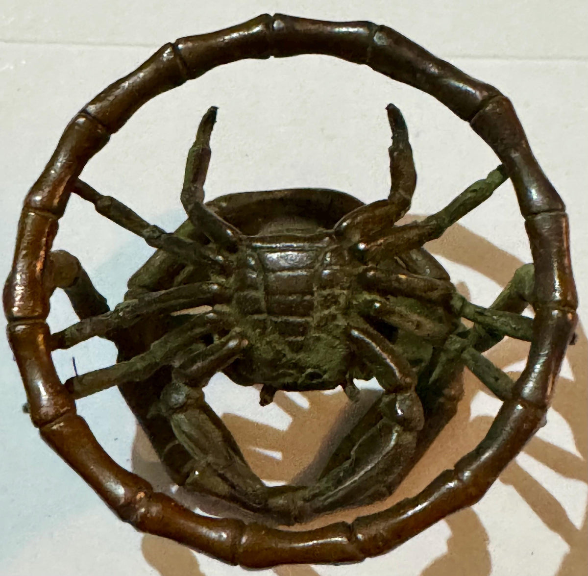 Bronze crab sculpture with curved horns inside bamboo-textured circular ring.