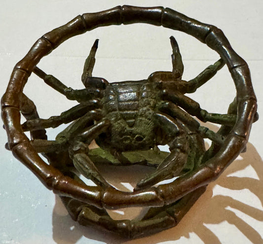Bronze crab sculpture with raised claws inside bamboo-textured ring, green patina finish.