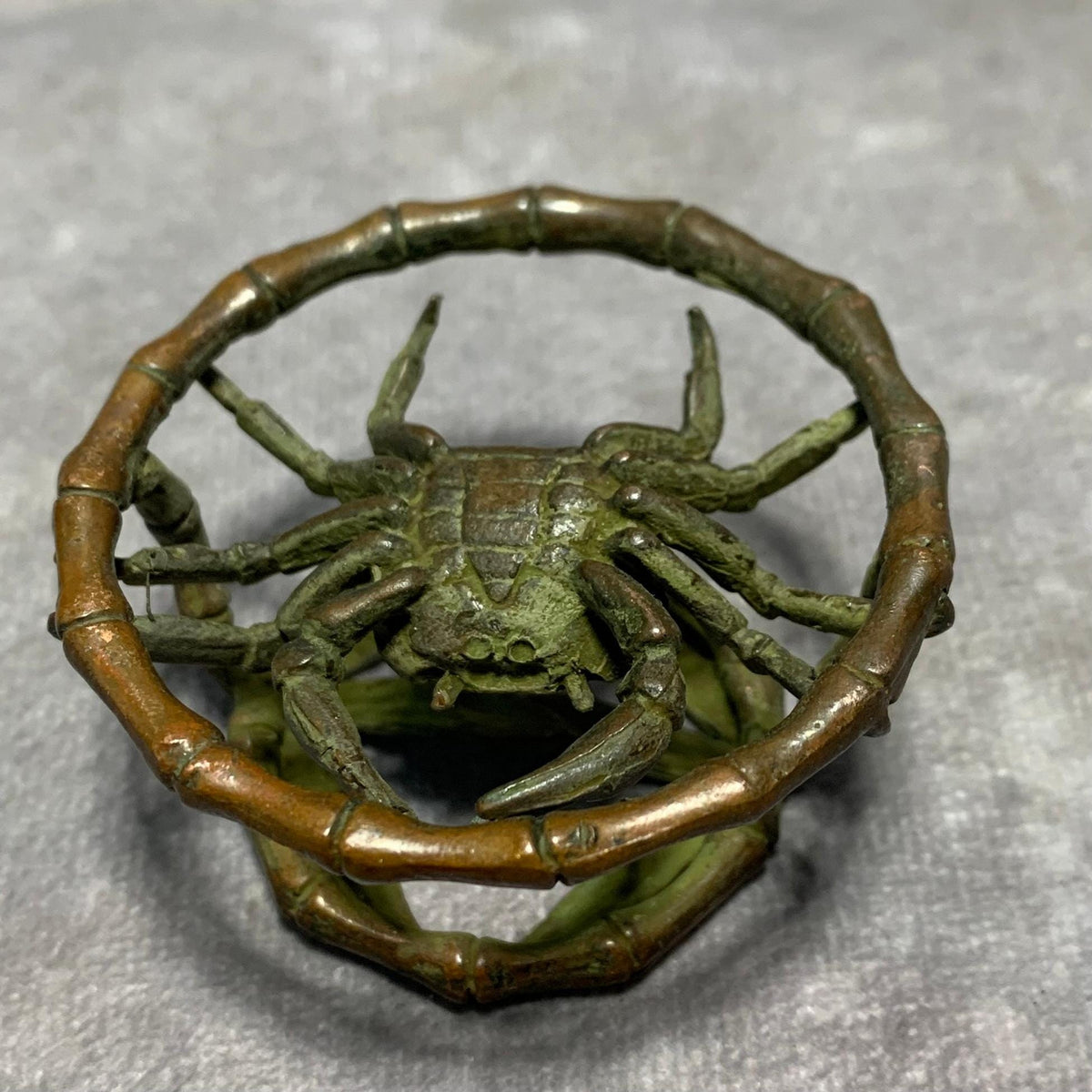 Bronze crab sculpture with extended legs inside patinated bamboo-style ring.