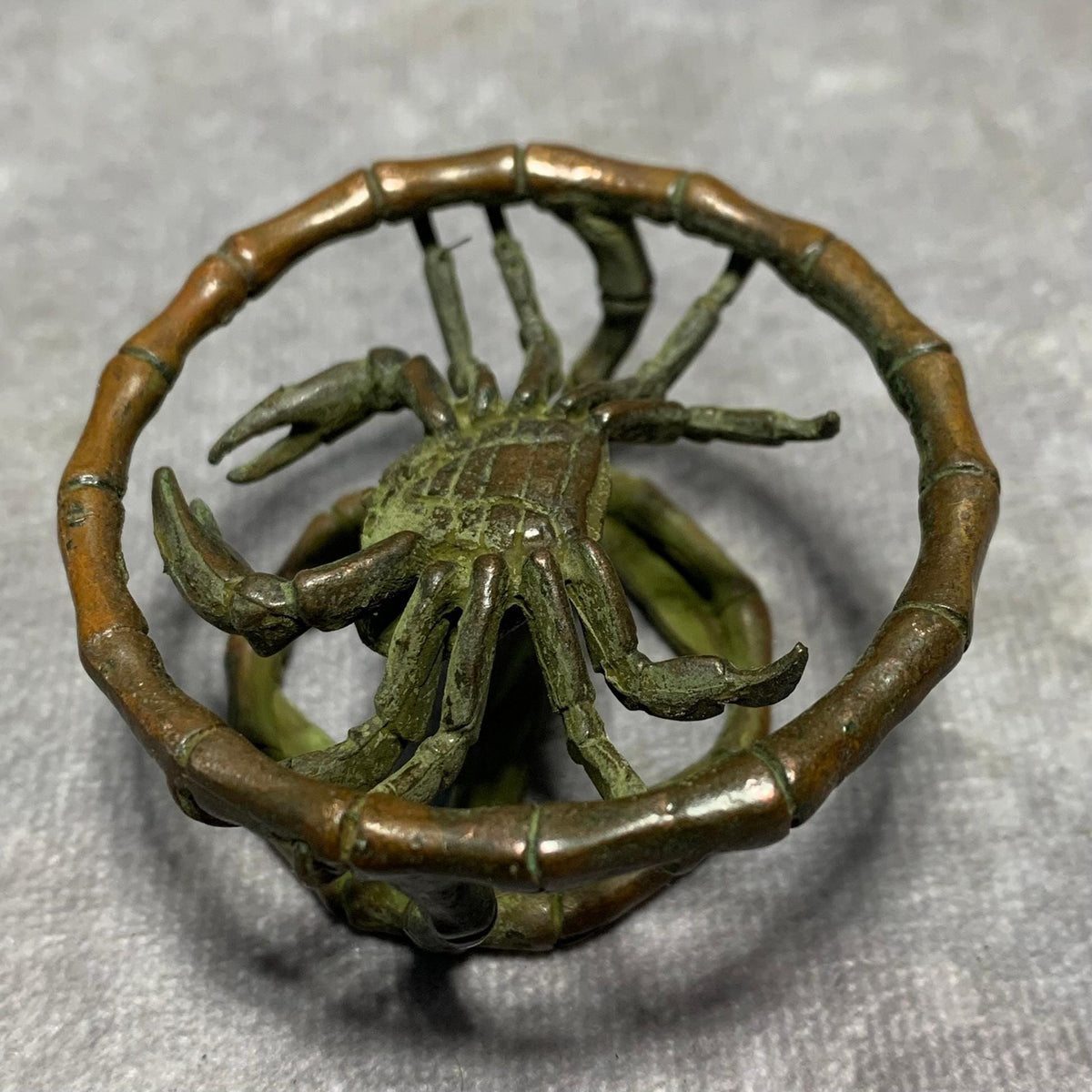 Bronze crab figurine with extended legs inside segmented bamboo ring.