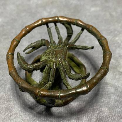 Bronze crab figurine with extended legs inside segmented bamboo ring.