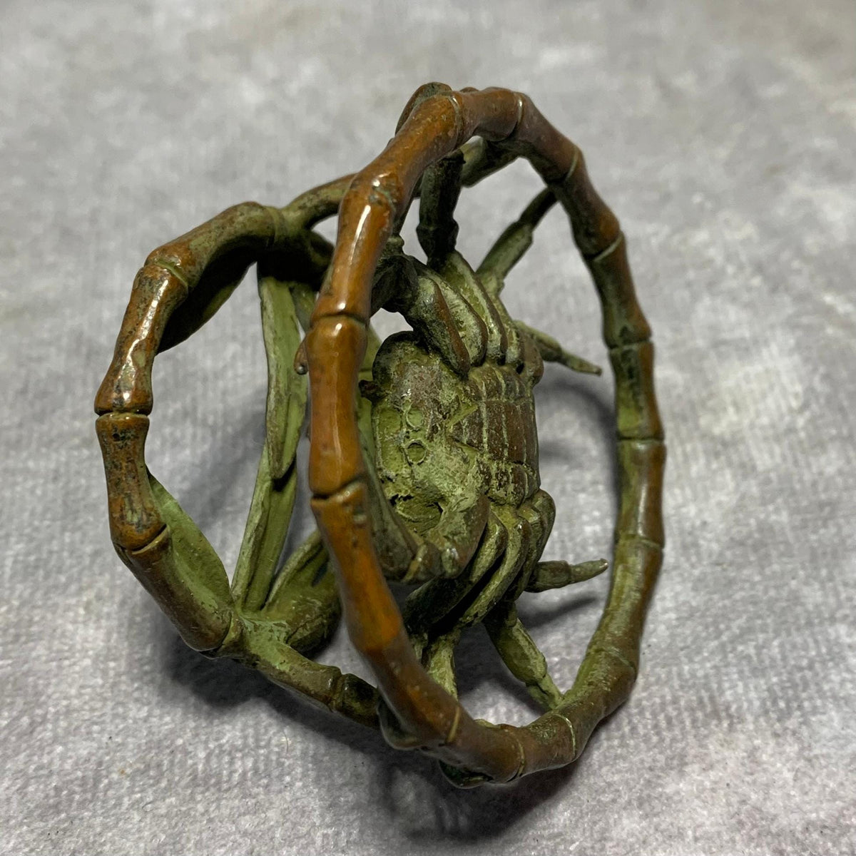 Vintage bronze crab ornament with green patina seated in bamboo ring.