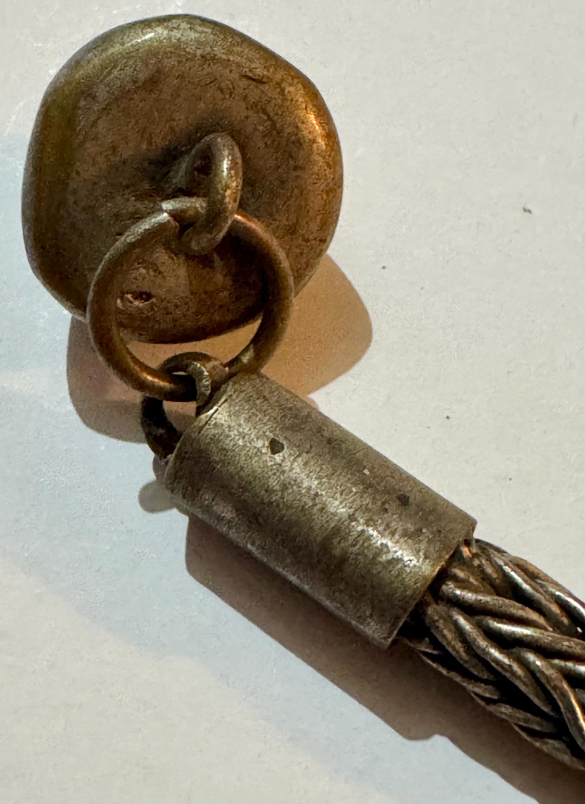 Antique brass dome ornament with ring attachment connected to twisted metal foxtail chain link.