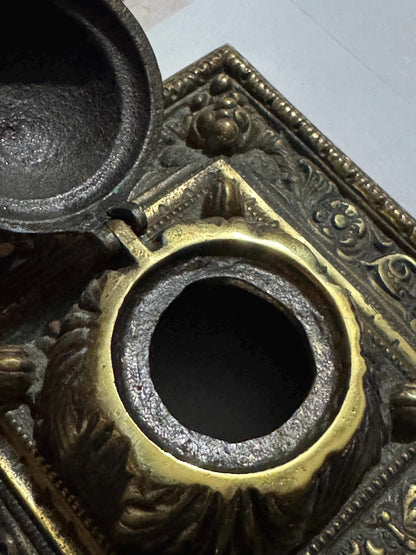 Both lids raised together on the brass double inkstand, showing the corner fruit-and-berry boss ornament and the unlined wells side by side
