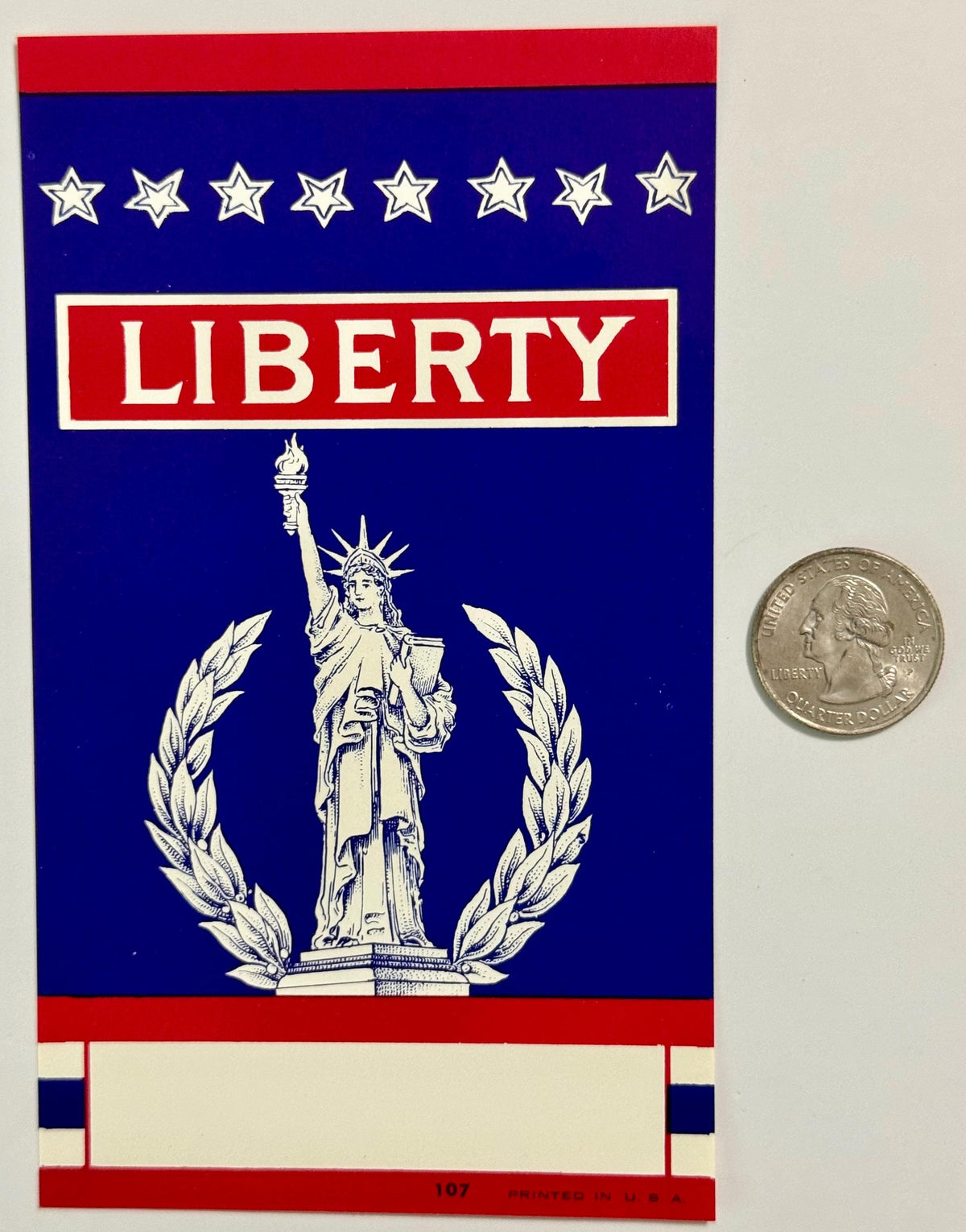 Vintage Liberty broom label with Statue of Liberty, eight stars, and laurel wreath on blue background, shown next to quarter 