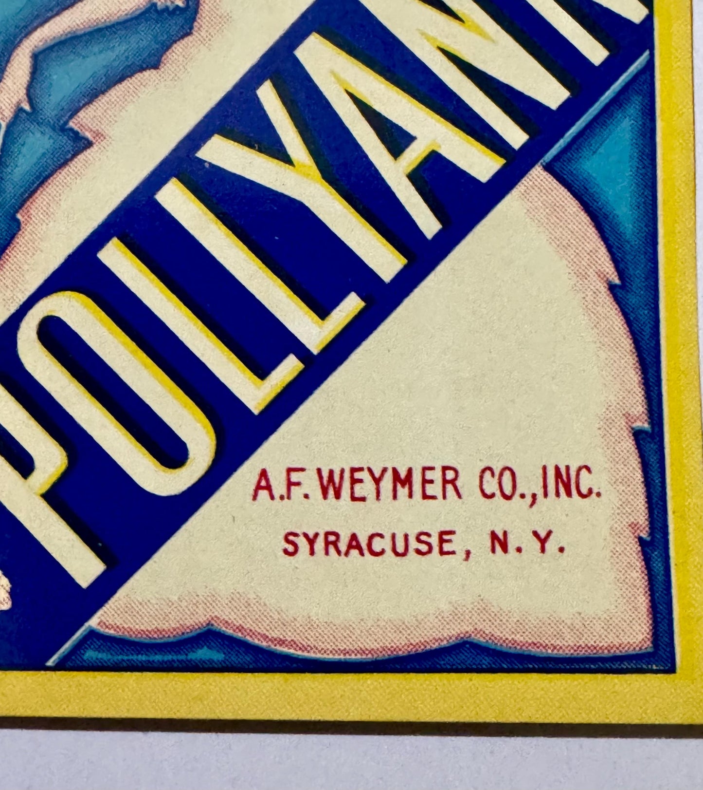Close-up of vintage broom label corner showing "A.F. Weymer Co., Inc. Syracuse, N.Y." in red text on cream background with bl