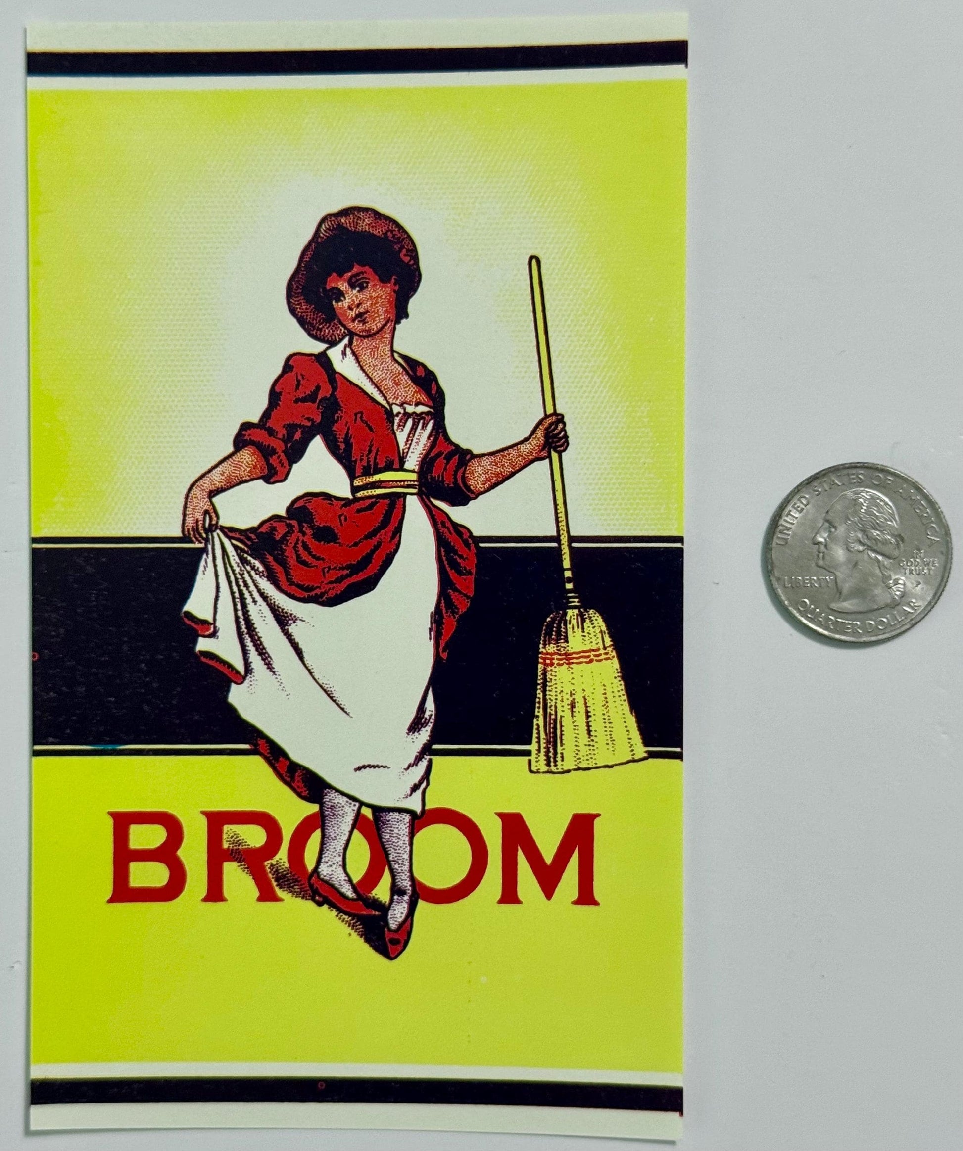 Vintage broom label with bright yellow-green background featuring a woman in red dress holding a broom, with "BROOM" text bel
