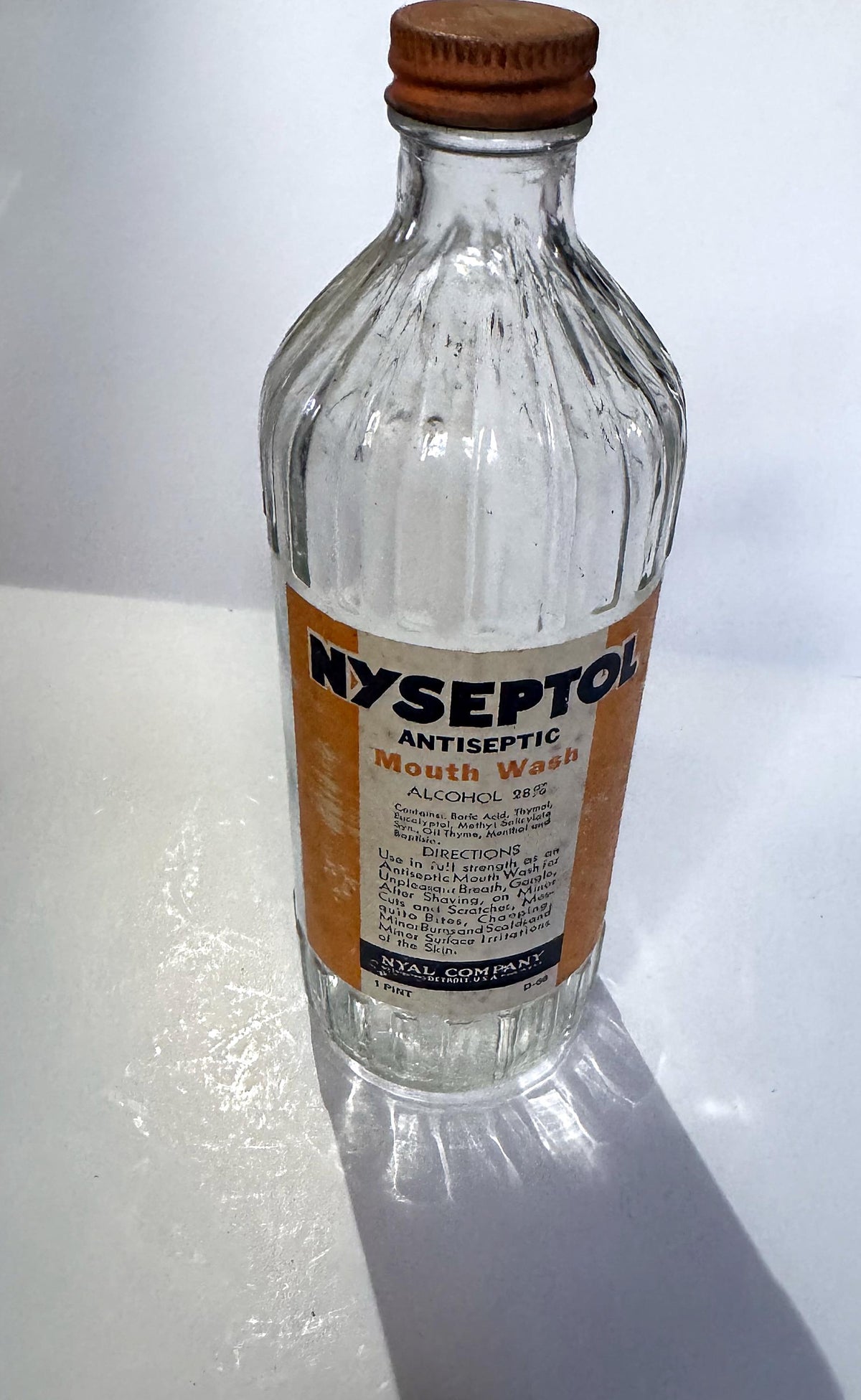 Nyseptol bottle standing upright, showing the vertical ribs on the glass shoulder and the orange NYAL screw cap