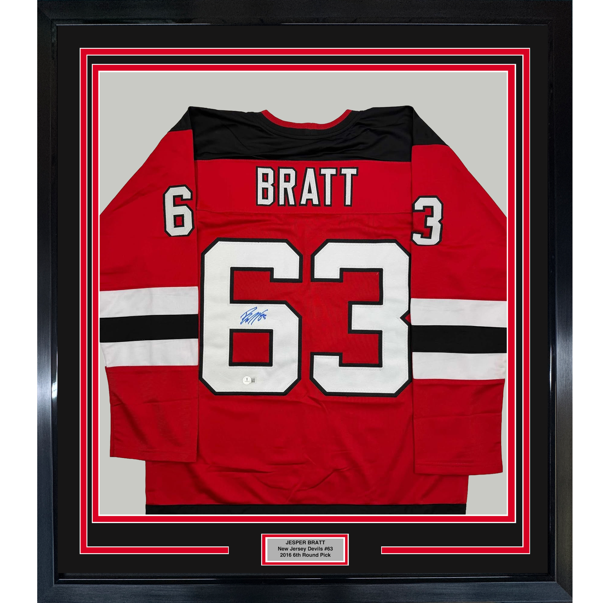 Framed red New Jersey Devils hockey jersey number 63 with "BRATT" nameplate and autograph, displayed flat against white matting with black border frame.