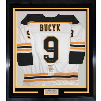 Framed white Boston Bruins jersey number 9 with "BUCYK" nameplate, signed with HOF 1981 inscription, black and orange striping, displayed front-facing in black frame with gold matting and authentication certificate.