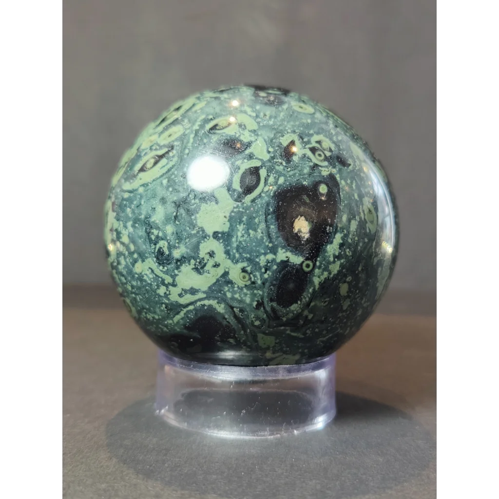 Kambaba jasper polished sphere sculpture with green and black swirling patterns displayed on a clear acrylic stand