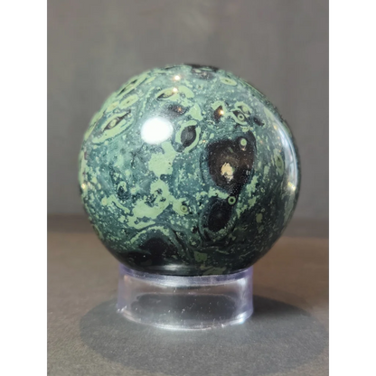 Kambaba jasper polished sphere sculpture with green and black swirling patterns displayed on a clear acrylic stand
