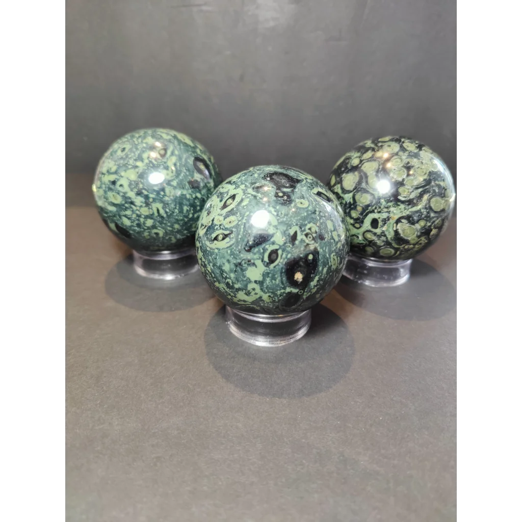Three green and black kambaba jasper polished sphere sculptures resting on clear acrylic stands