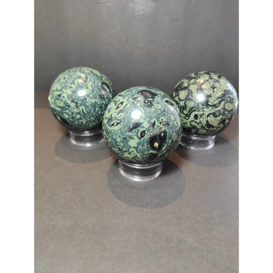 Three green and black kambaba jasper polished sphere sculptures resting on clear acrylic stands