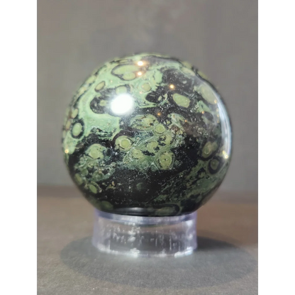 Kambaba jasper polished sphere sculpture with green and black patterns displayed on a clear acrylic stand