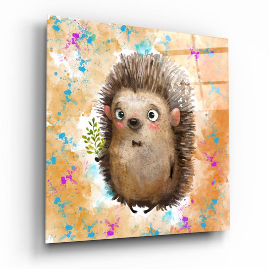 Glass wall art panel displaying a wide-eyed hedgehog illustration with colorful paint splatters on warm tan and orange background, angled three-quarter view.