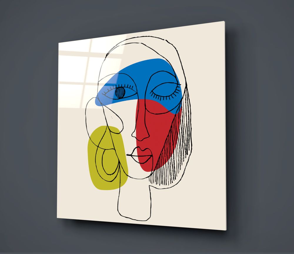 Modern glass wall art displaying an abstract line-drawn face with blue, red, and yellow colored sections mounted at an angle against a gray wall.